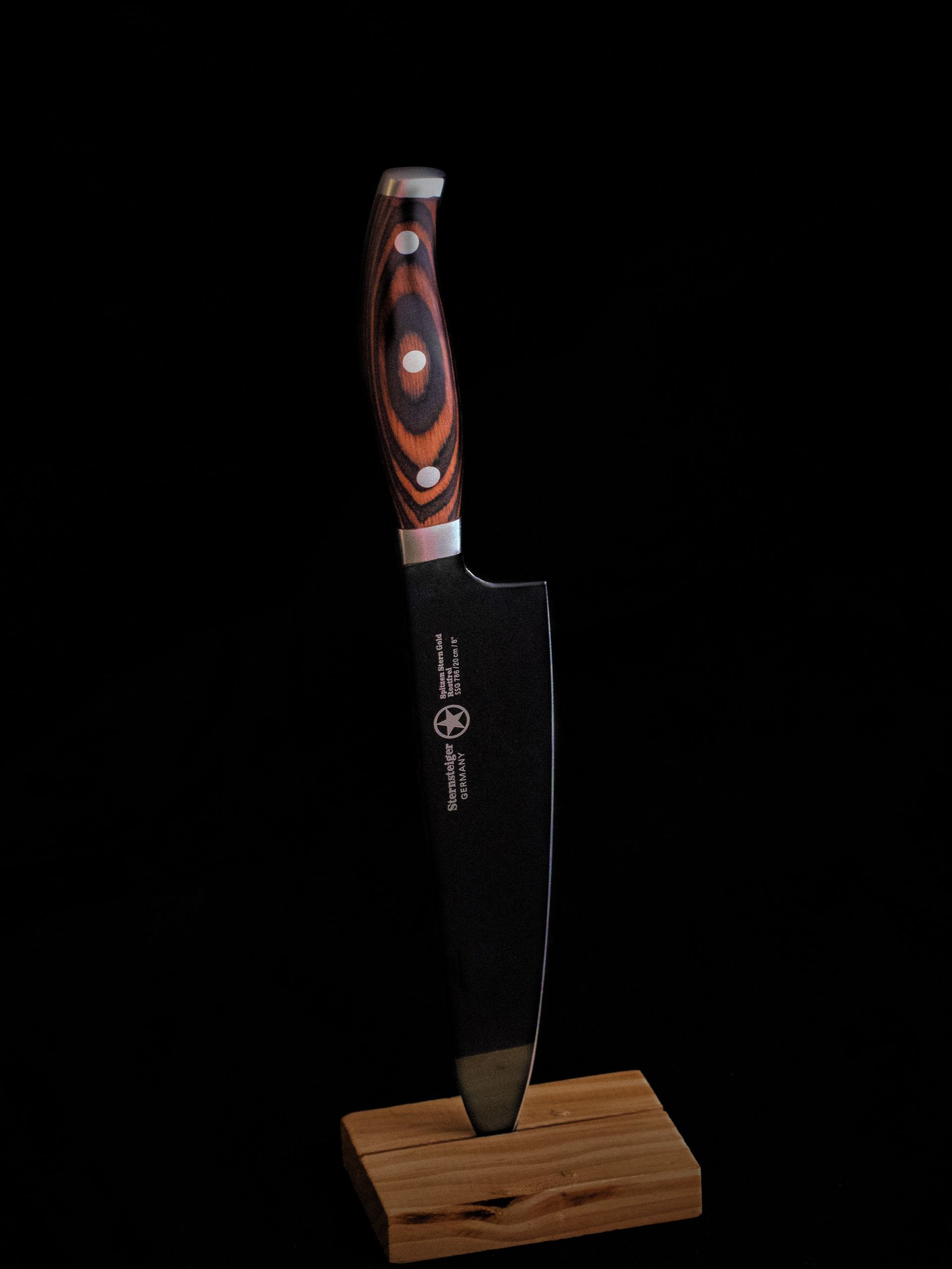 A sharp chef's knife displayed vertically against a black background.