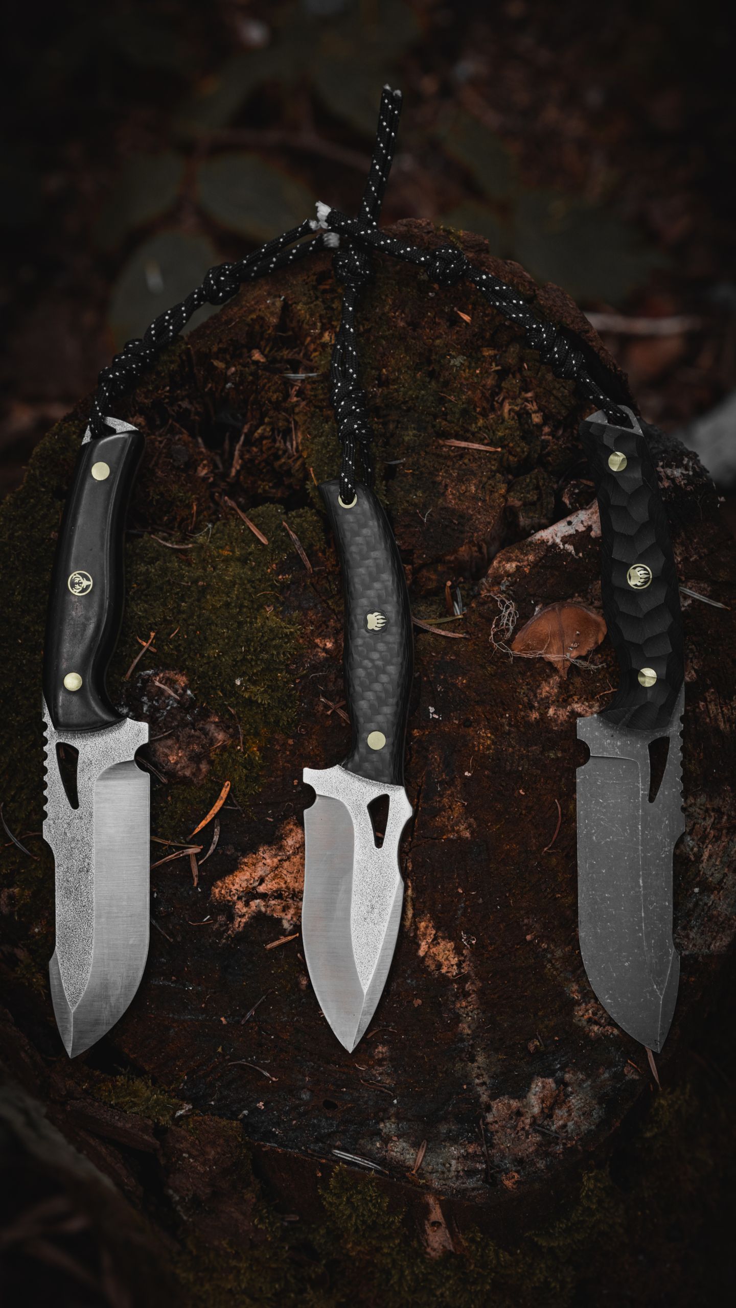 Three tactical knives displayed on a moss-covered stump, showcasing outdoor survival tools.